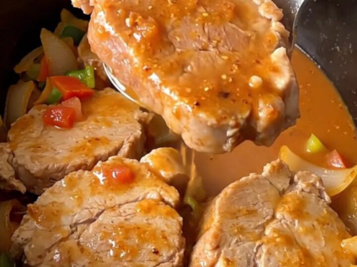 A close-up of tender, slow-cooked pork loin slices covered in a thick, savory vegetable gravy in a slow cooker.