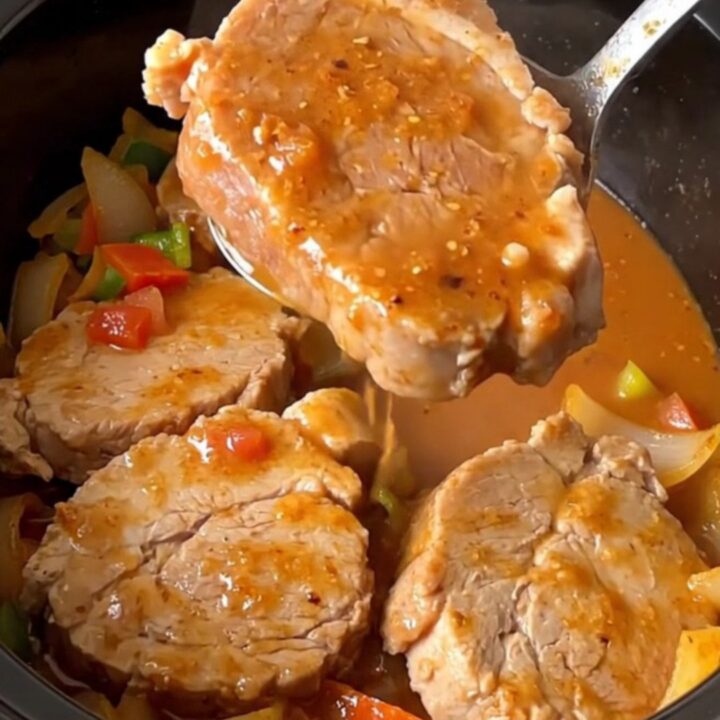A close-up of tender, slow-cooked pork loin slices covered in a thick, savory vegetable gravy in a slow cooker.