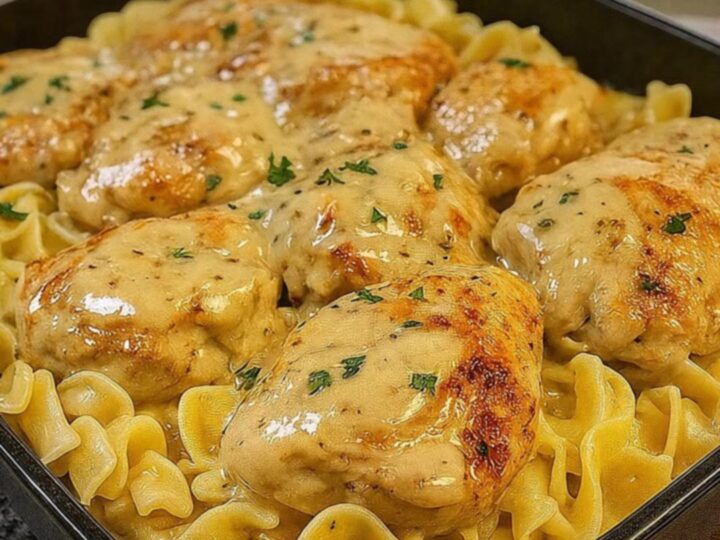 A square black pan filled with golden seared chicken cutlets resting over creamy, glossy egg noodles.