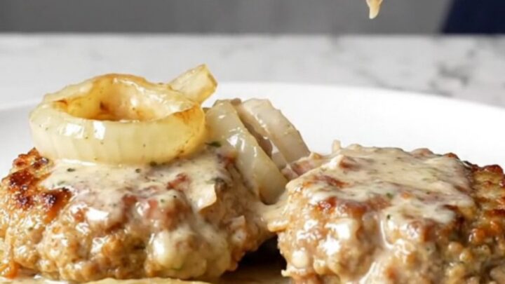 Four golden-tan turkey burger steaks covered in a rich creamy onion gravy inside a black slow cooker insert.