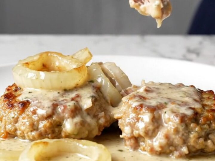 Four golden-tan turkey burger steaks covered in a rich creamy onion gravy inside a black slow cooker insert.
