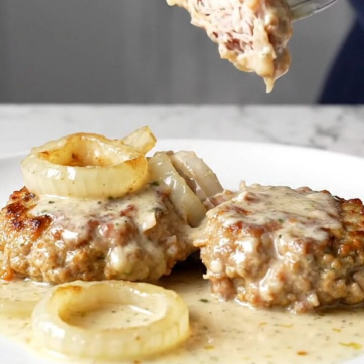 Four golden-tan turkey burger steaks covered in a rich creamy onion gravy inside a black slow cooker insert.