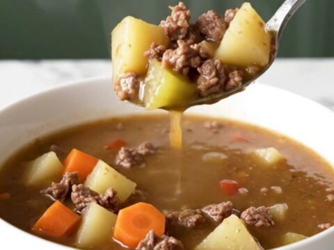 A steaming bowl of Kansas City steak soup with browned beef, potato cubes, carrots, and celery in a rich brown broth.
