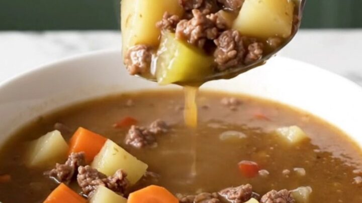 A steaming bowl of Kansas City steak soup with browned beef, potato cubes, carrots, and celery in a rich brown broth.