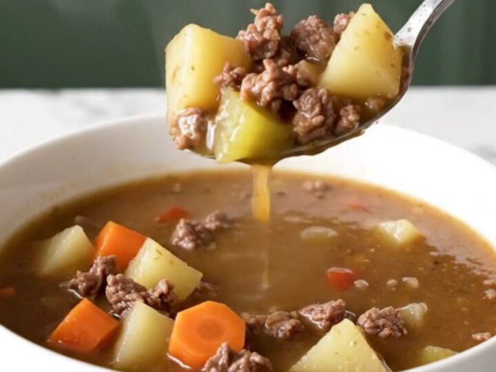 A steaming bowl of Kansas City steak soup with browned beef, potato cubes, carrots, and celery in a rich brown broth.