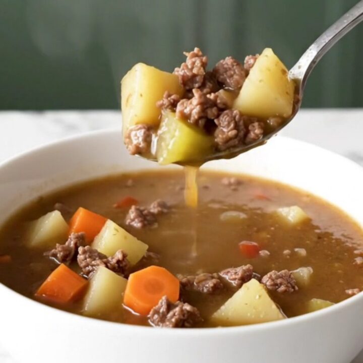 A steaming bowl of Kansas City steak soup with browned beef, potato cubes, carrots, and celery in a rich brown broth.