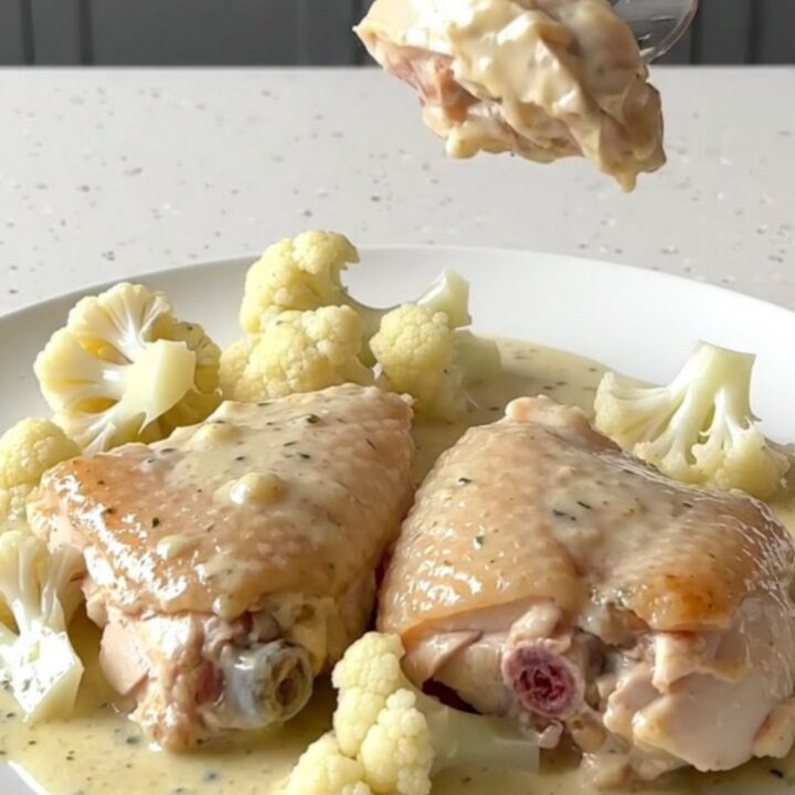 Creamy chicken Alfredo thighs with cauliflower in a black slow cooker insert.