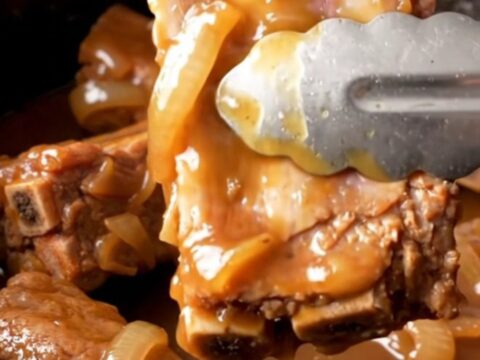A close-up of tender, whiskey-glazed spareribs in a slow cooker, with a golden-tan color and soft onion slices visible.