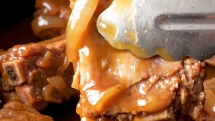 A close-up of tender, whiskey-glazed spareribs in a slow cooker, with a golden-tan color and soft onion slices visible.