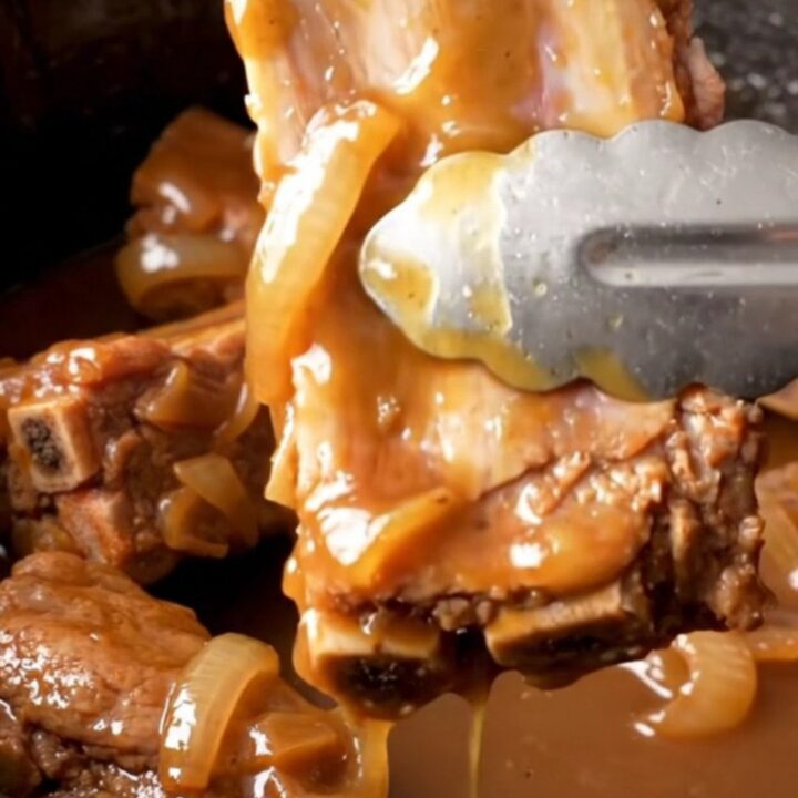 A close-up of tender, whiskey-glazed spareribs in a slow cooker, with a golden-tan color and soft onion slices visible.