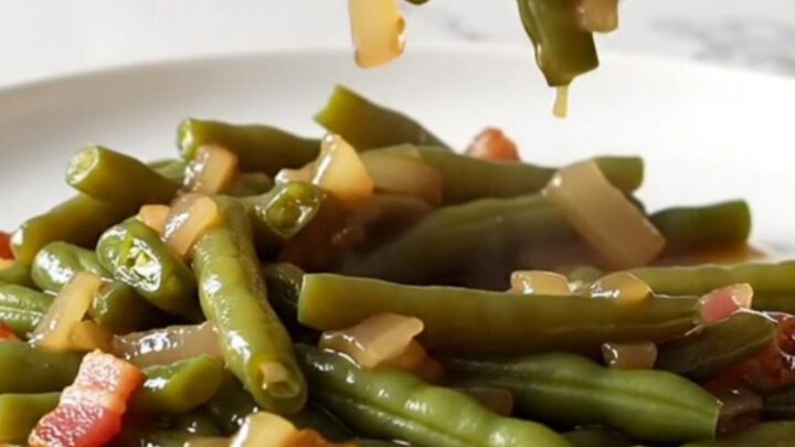 A close-up of tender, olive-green beans mixed with bacon and onions in a rich amber sauce.