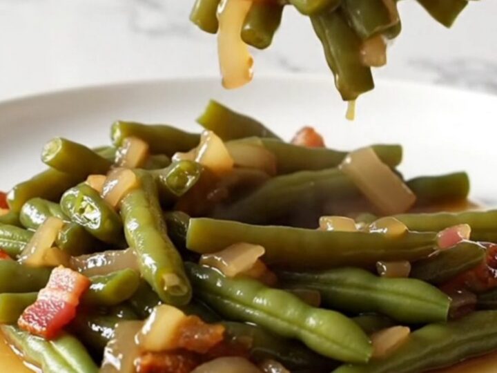 A close-up of tender, olive-green beans mixed with bacon and onions in a rich amber sauce.