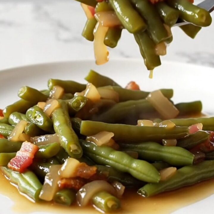 A close-up of tender, olive-green beans mixed with bacon and onions in a rich amber sauce.