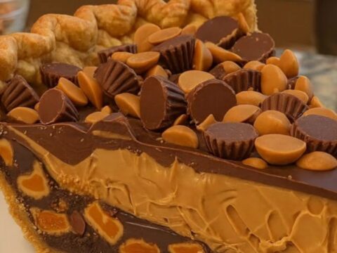 A tall, perfect slice of peanut butter pie on a white plate showing distinct layers of crust, peanut butter, and chocolate.
