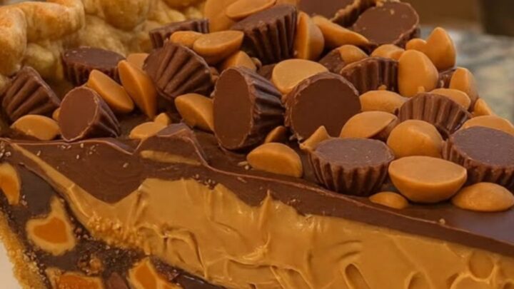 A tall, perfect slice of peanut butter pie on a white plate showing distinct layers of crust, peanut butter, and chocolate.