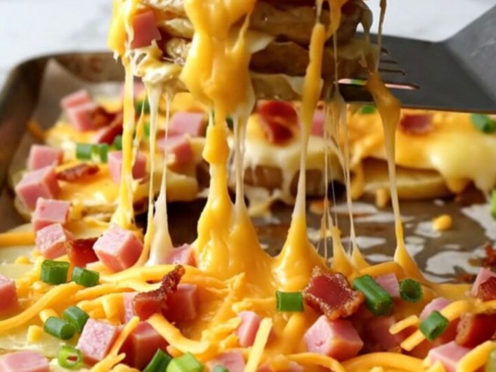 A sheet pan filled with golden, crispy potato rounds topped with melted cheddar, ham cubes, and bacon bits.