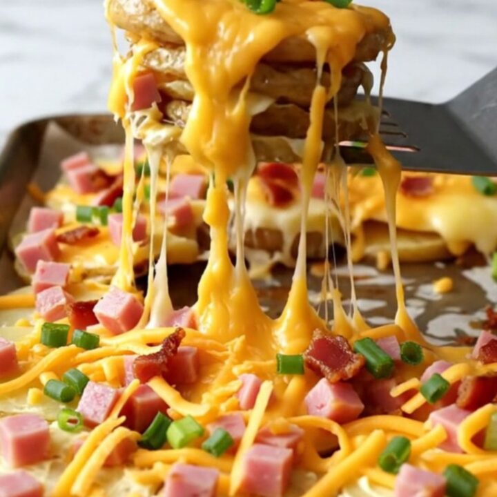 A sheet pan filled with golden, crispy potato rounds topped with melted cheddar, ham cubes, and bacon bits.