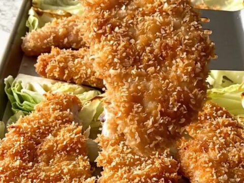 A golden-brown panko-crusted chicken cutlet next to roasted cabbage wedges on a sheet pan.