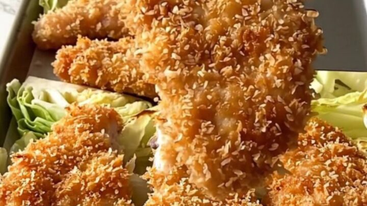 A golden-brown panko-crusted chicken cutlet next to roasted cabbage wedges on a sheet pan.
