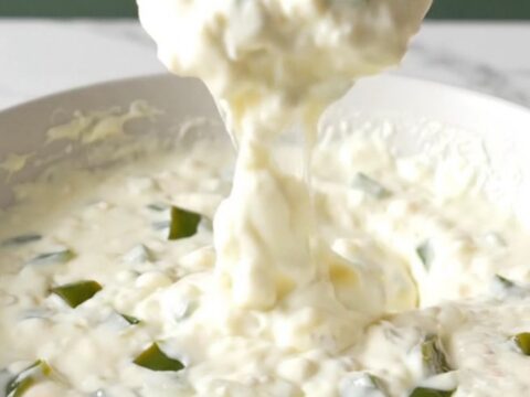 A bowl of creamy white queso with visible bits of roasted poblano peppers, ready for dipping.