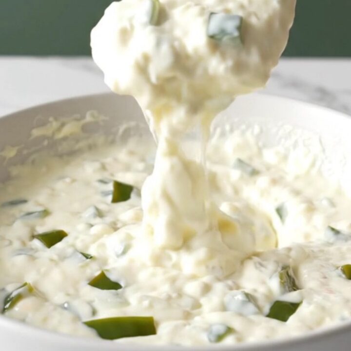 A bowl of creamy white queso with visible bits of roasted poblano peppers, ready for dipping.