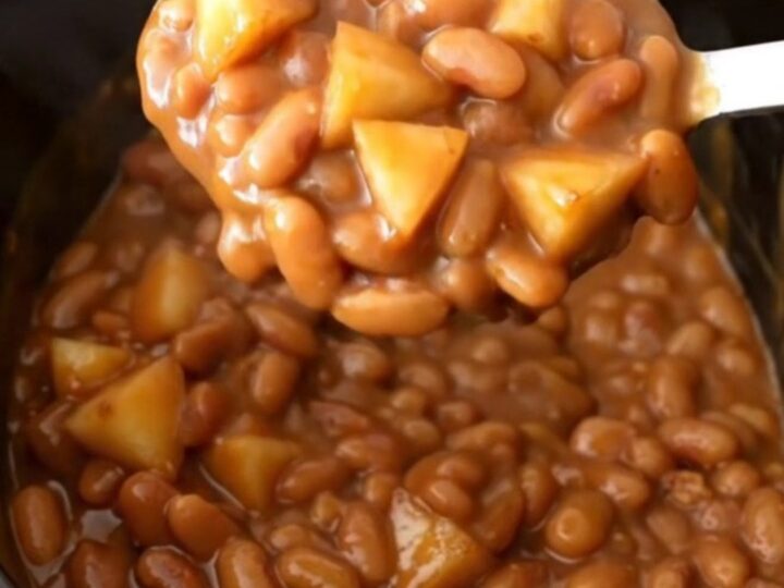 A close-up view of slow cooker apple bacon baked beans in a black stoneware insert, showing a rich brown texture.