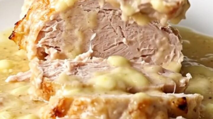 A cooked, sliced turkey breast with a creamy sauce on a white plate.