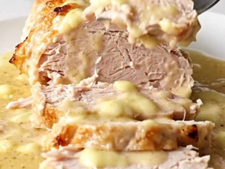 A cooked, sliced turkey breast with a creamy sauce on a white plate.