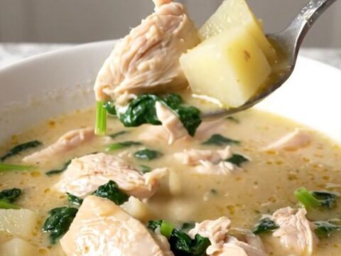 A bowl of creamy spanakopita chicken soup with visible chicken chunks, potato cubes, and spinach.