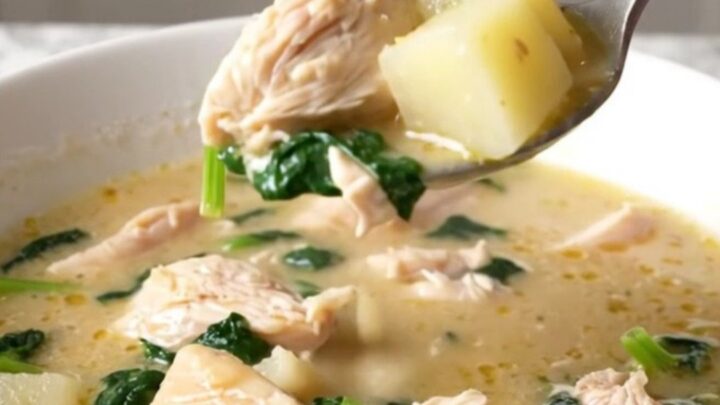 A bowl of creamy spanakopita chicken soup with visible chicken chunks, potato cubes, and spinach.