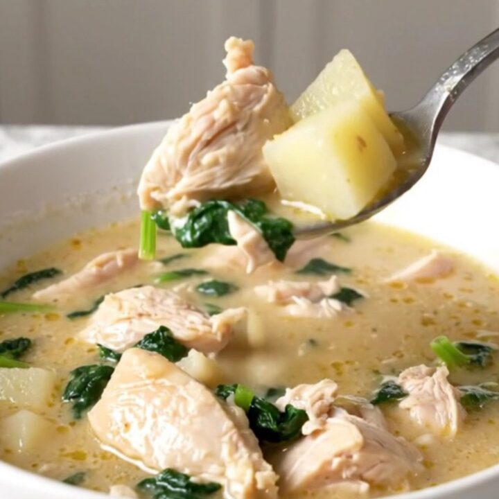 A bowl of creamy spanakopita chicken soup with visible chicken chunks, potato cubes, and spinach.