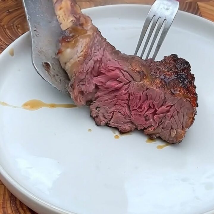 A perfectly seared tomahawk ribeye steak resting on a wooden butcher block with a crisp, charred exterior.