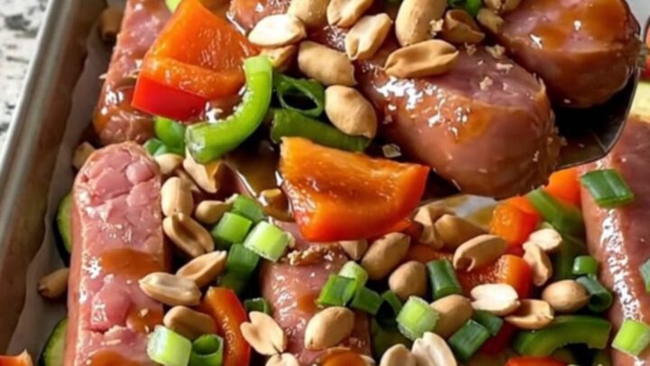 A sheet pan filled with golden-brown kielbasa coins, vibrant bell peppers, and zucchini tossed in a rich kung pao sauce.
