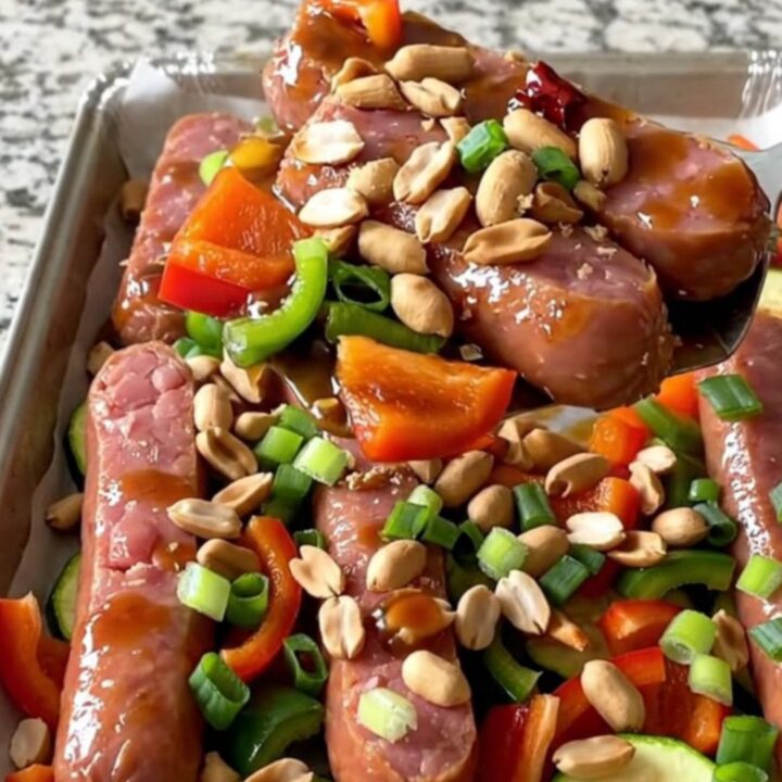 A sheet pan filled with golden-brown kielbasa coins, vibrant bell peppers, and zucchini tossed in a rich kung pao sauce.