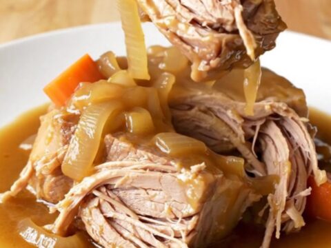 A rustic pork shoulder roast braised in a rich brown gravy with carrots and onions in a slow cooker.