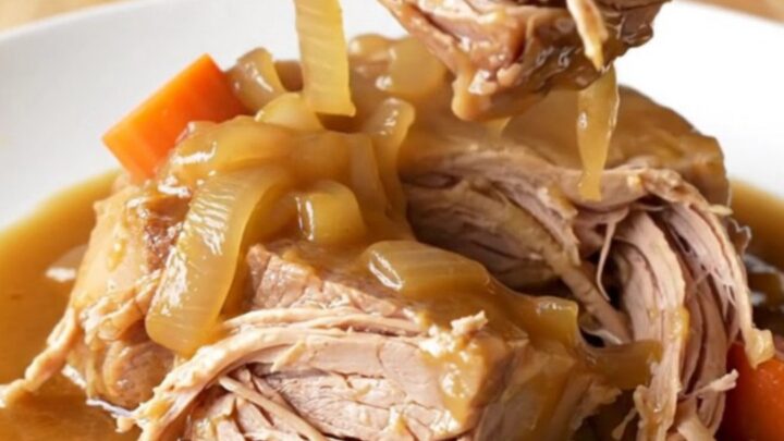 A rustic pork shoulder roast braised in a rich brown gravy with carrots and onions in a slow cooker.