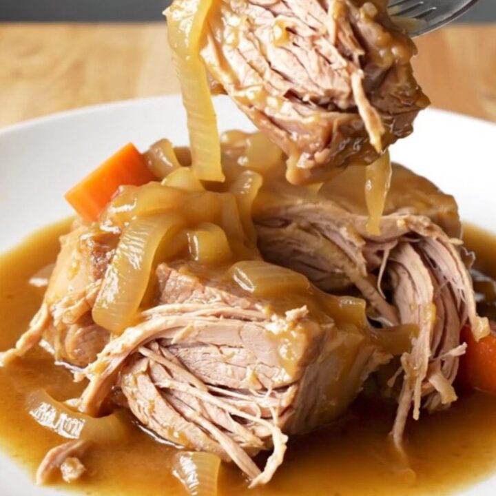 A rustic pork shoulder roast braised in a rich brown gravy with carrots and onions in a slow cooker.