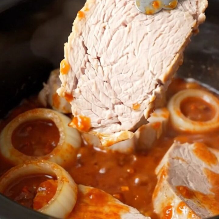 Close-up of tender honey chili crisp pork chops in a slow cooker, coated in a thick red sauce.
