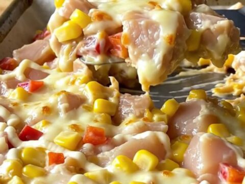A sheet pan filled with golden, melted mozzarella cheese over cooked chicken chunks, corn, and red peppers.