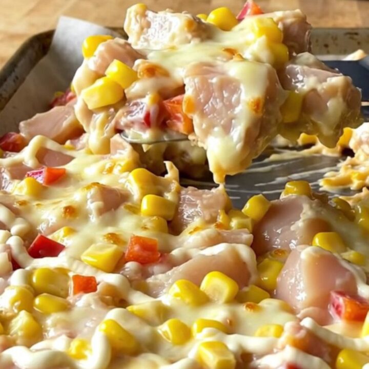 A sheet pan filled with golden, melted mozzarella cheese over cooked chicken chunks, corn, and red peppers.