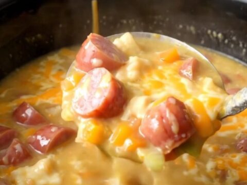 A close-up of a slow cooker filled with creamy kielbasa and potato soup, garnished with a light dusting of smoked paprika.