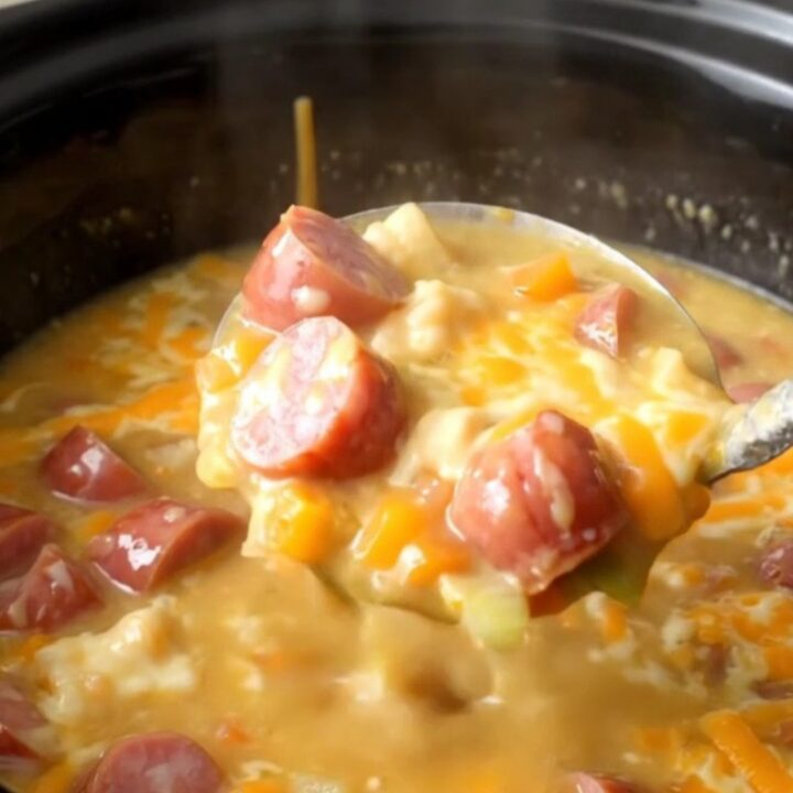 A close-up of a slow cooker filled with creamy kielbasa and potato soup, garnished with a light dusting of smoked paprika.
