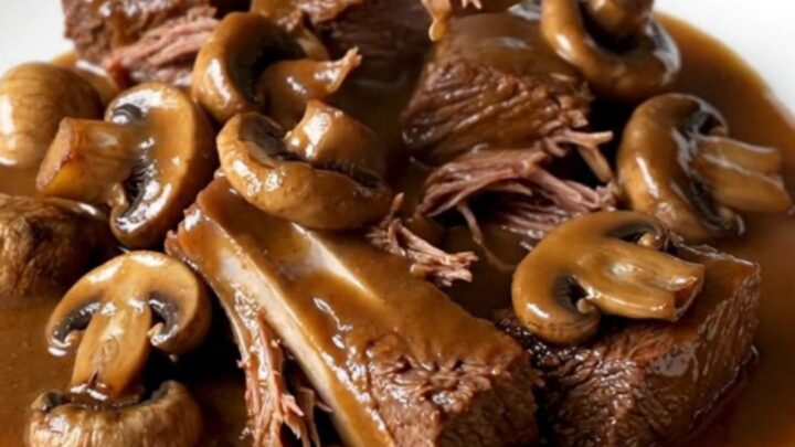 A close-up of tender brown beef tips and whole mushrooms in a rich gravy inside a black slow cooker.
