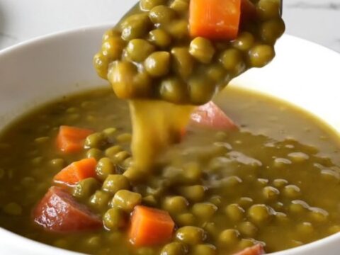 A close-up of a slow cooker filled with kielbasa coins, split peas, and diced carrots in a savory broth.
