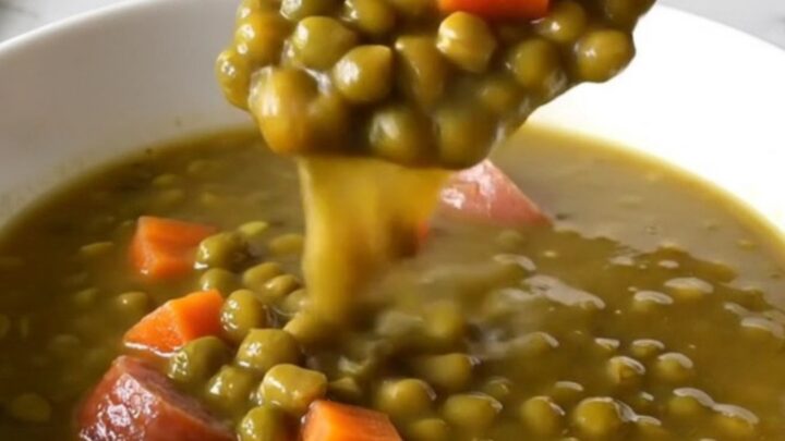 A close-up of a slow cooker filled with kielbasa coins, split peas, and diced carrots in a savory broth.