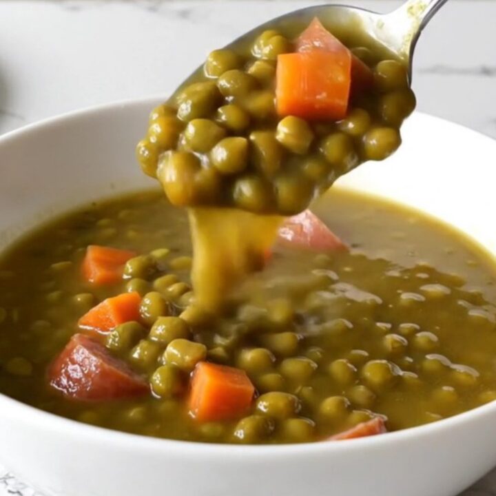A close-up of a slow cooker filled with kielbasa coins, split peas, and diced carrots in a savory broth.
