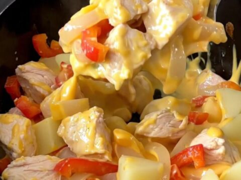 A close-up of a slow cooker filled with cooked chicken, peppers, and potatoes in a creamy cheese sauce.