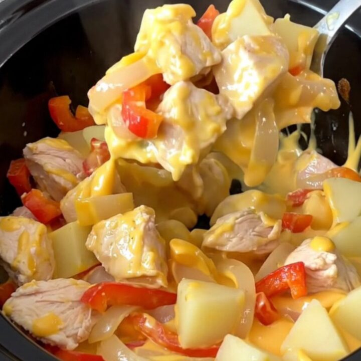 A close-up of a slow cooker filled with cooked chicken, peppers, and potatoes in a creamy cheese sauce.