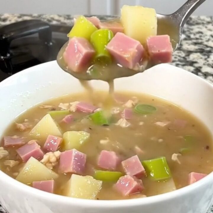 A close-up of the slow cooker filled with diced ham, leeks, and cubed potatoes in a golden broth.