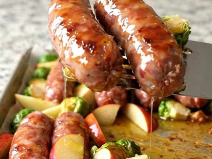 A sheet pan filled with golden-brown Italian sausage, roasted Brussels sprouts, and caramelized apple wedges.
